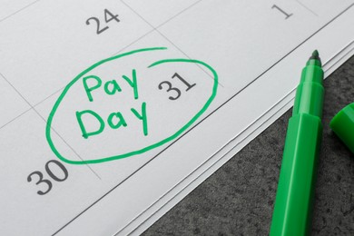 Photo of Calendar page with marked payday date and green marker on table, closeup