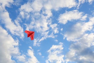 Image of Red paper plane flying in blue sky with clouds