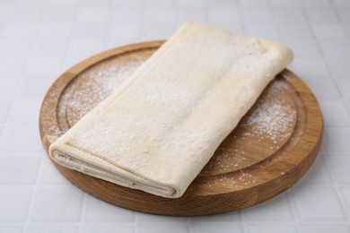 Photo of Raw puff pastry dough on white tiled table, closeup