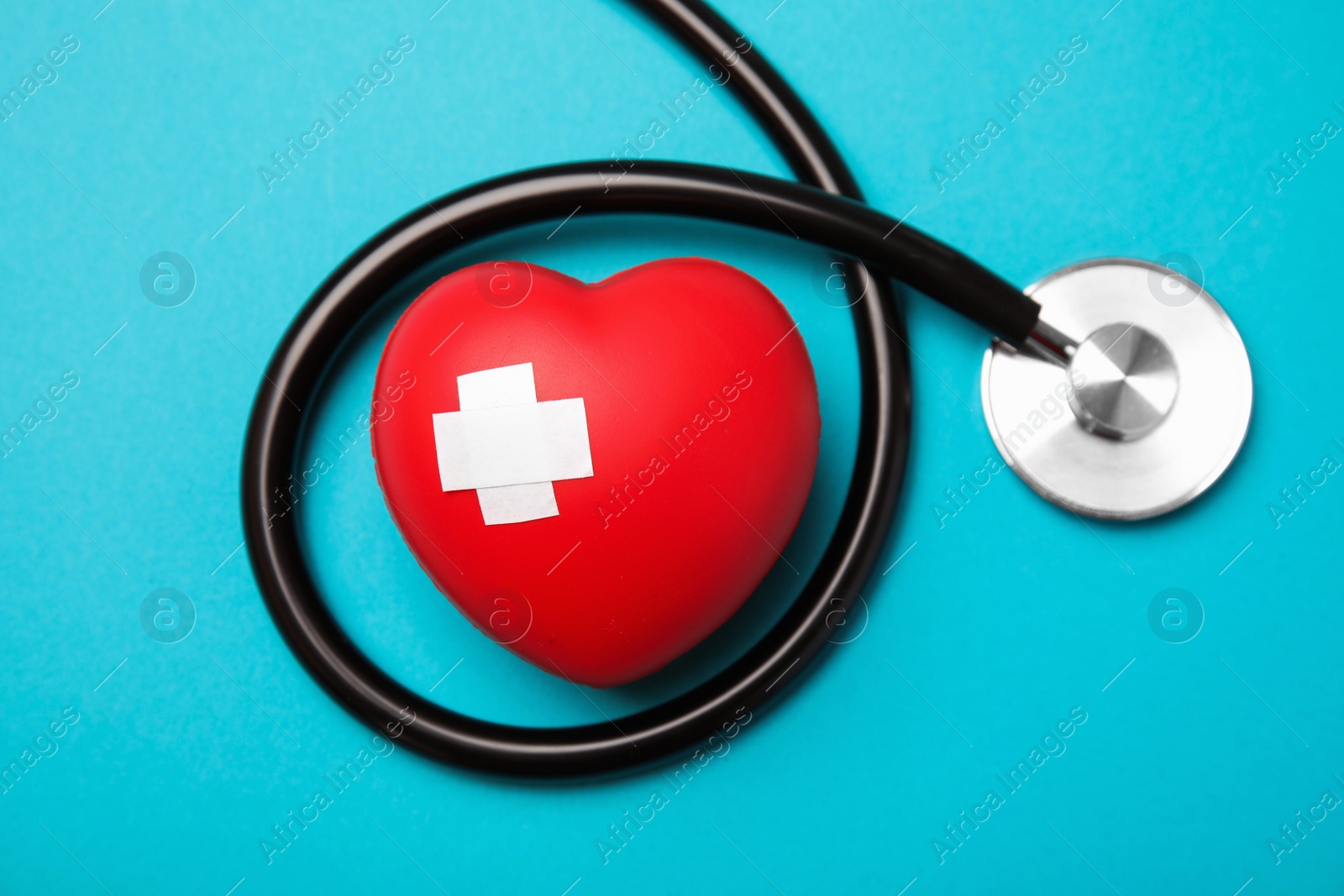 Photo of Stethoscope and red heart with adhesive plasters on color background, top view. Cardiology concept
