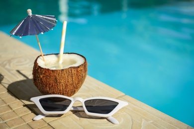 Photo of Tasty tropical cocktail and sunglasses on edge of swimming pool. Party items
