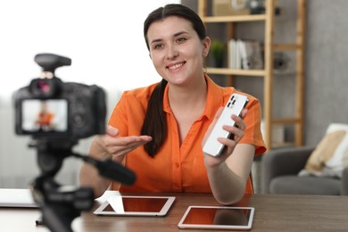 Photo of Smiling technology blogger with smartphone recording video review at home