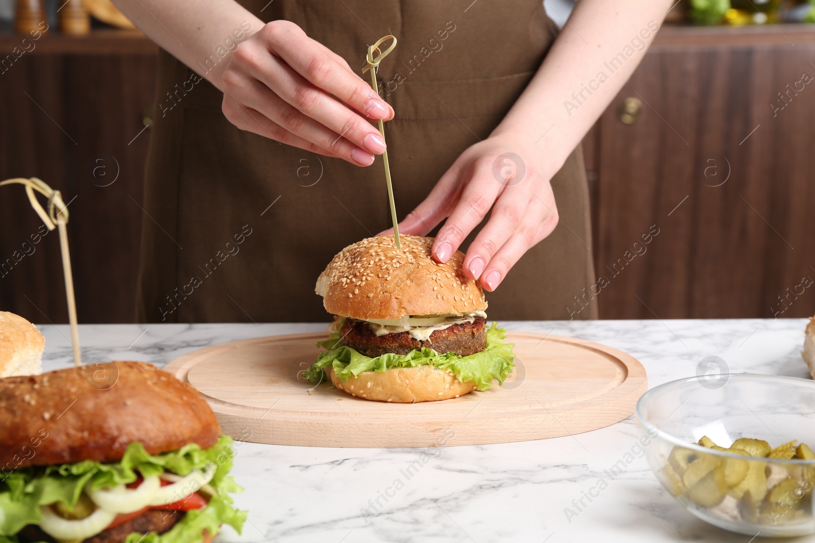 Photo of Woman making delicious vegetarian burger at white marble table, closeup