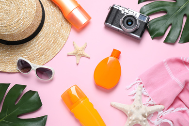 Flat lay composition with sun protection products and beach accessories on pink background