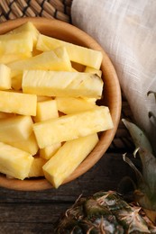 Photo of Pieces of tasty ripe pineapple in bowl on wooden table, top view