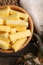 Pieces of tasty ripe pineapple in bowl on wooden table, top view