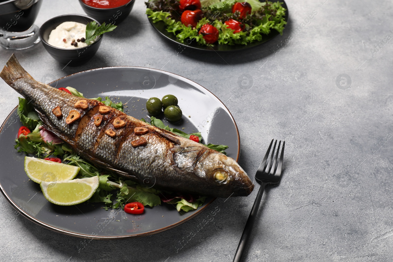 Photo of Delicious sea bass fish and ingredients served on light grey table