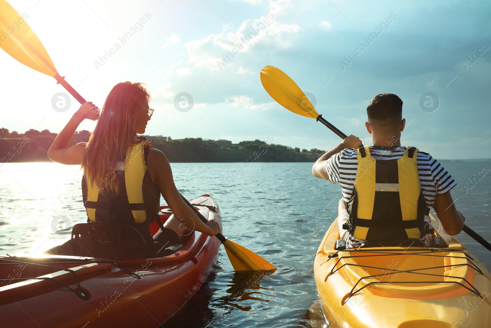 Photo of Couple in life jackets kayaking on river, back view. Summer activity