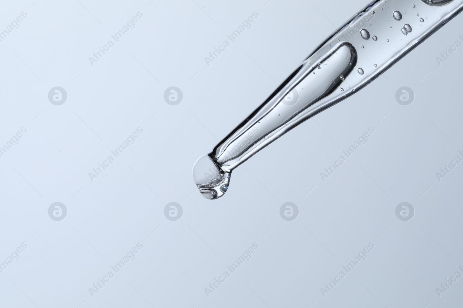 Photo of Dripping liquid from pipette on light blue background, closeup. Space for text