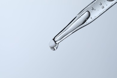 Photo of Dripping liquid from pipette on light blue background, closeup. Space for text