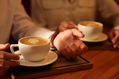 Photo of Couple with cups of aromatic coffee at wooden table, closeup