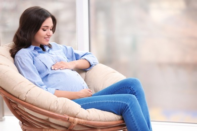 Beautiful pregnant woman sitting in lounge chair near window