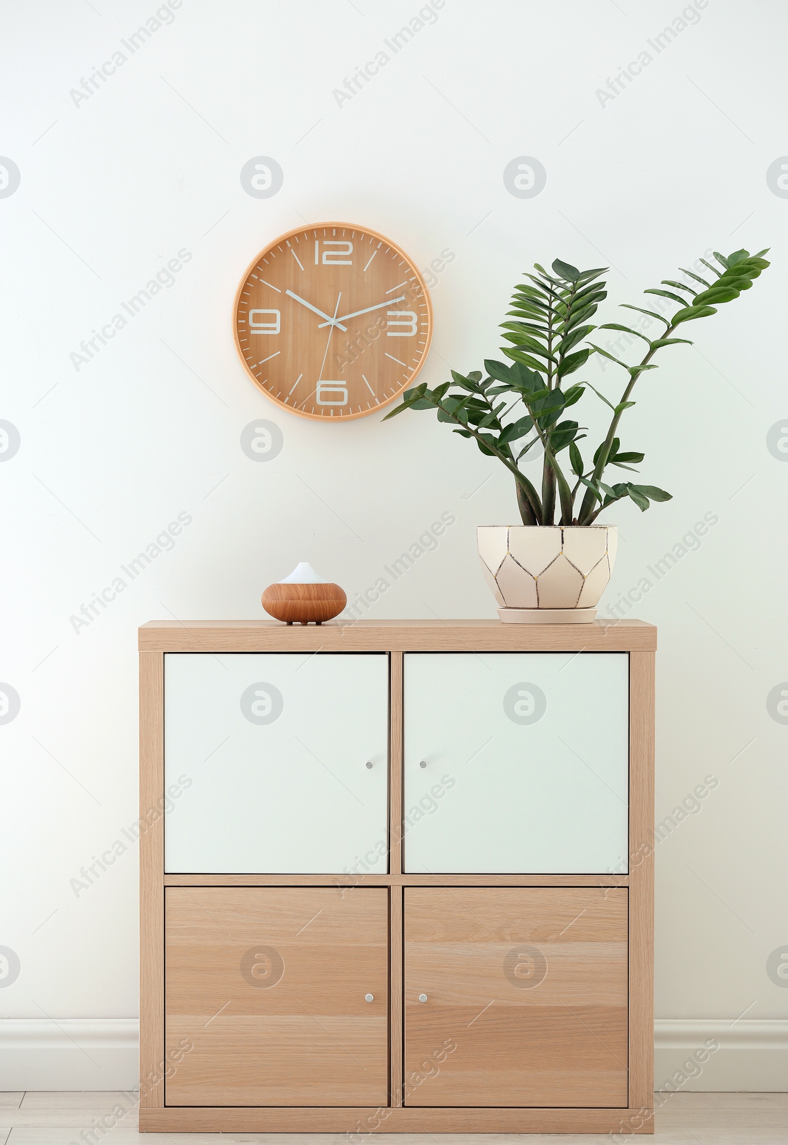 Photo of Aroma oil diffuser lamp and plant on cabinet against white wall