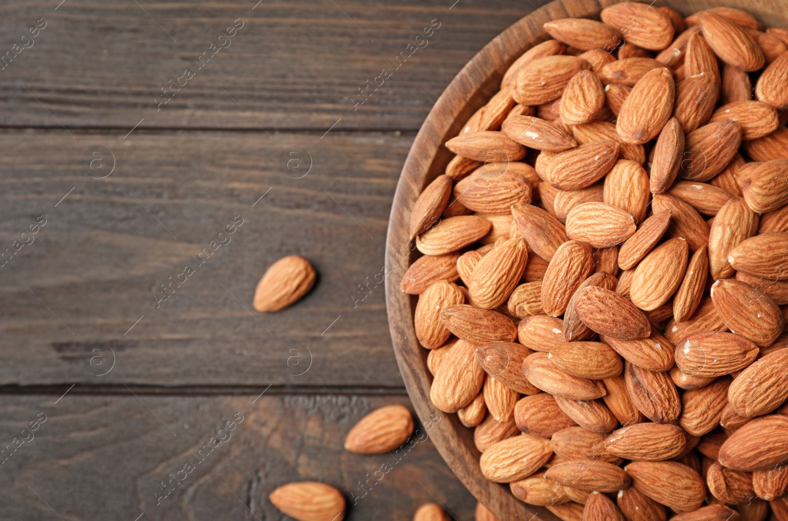 Photo of Tasty organic almond nuts in bowl and space for text on table, top view