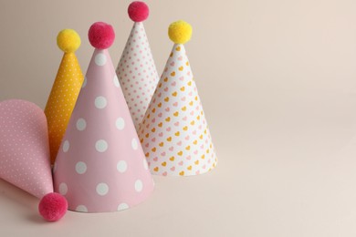 Photo of Beautiful party hats with pompoms on beige background. Space for text