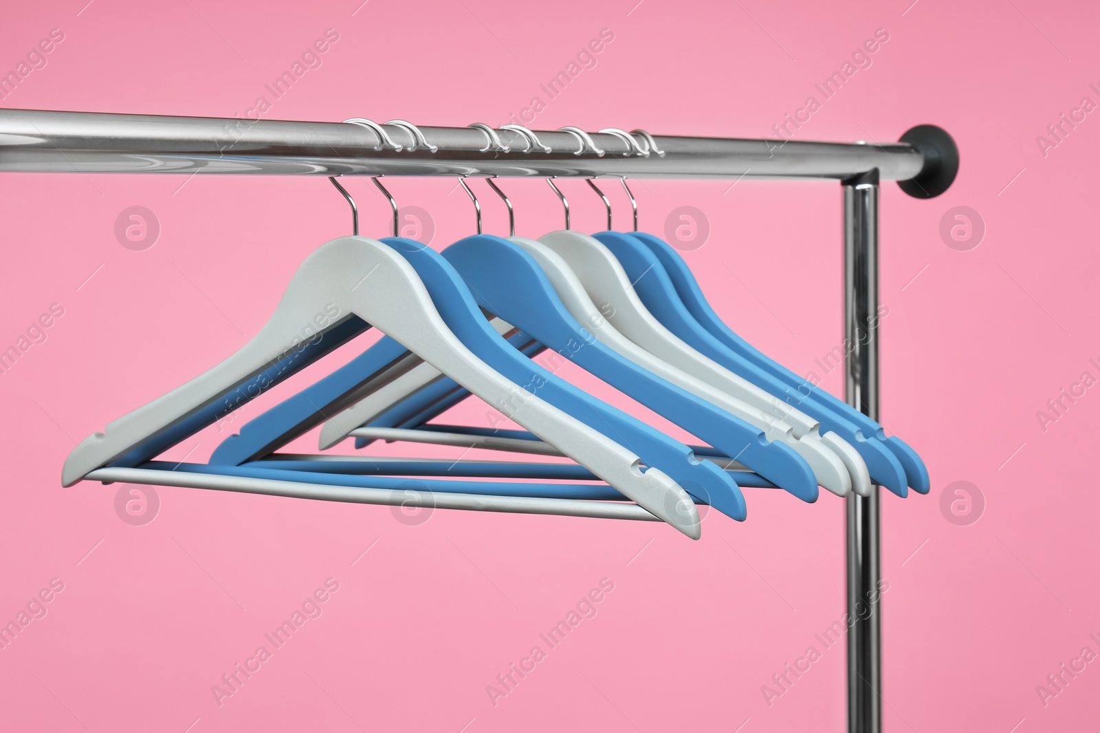 Photo of Empty clothes hangers on metal rack against color background