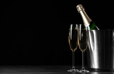 Glasses of champagne near bucket with bottle on black background, space for text