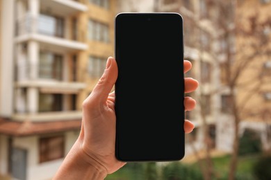 Photo of Woman holding smartphone with blank screen near building outdoors, closeup