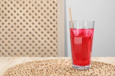 Photo of Glass of red soda water with ice cubes and straw on wooden table, space for text