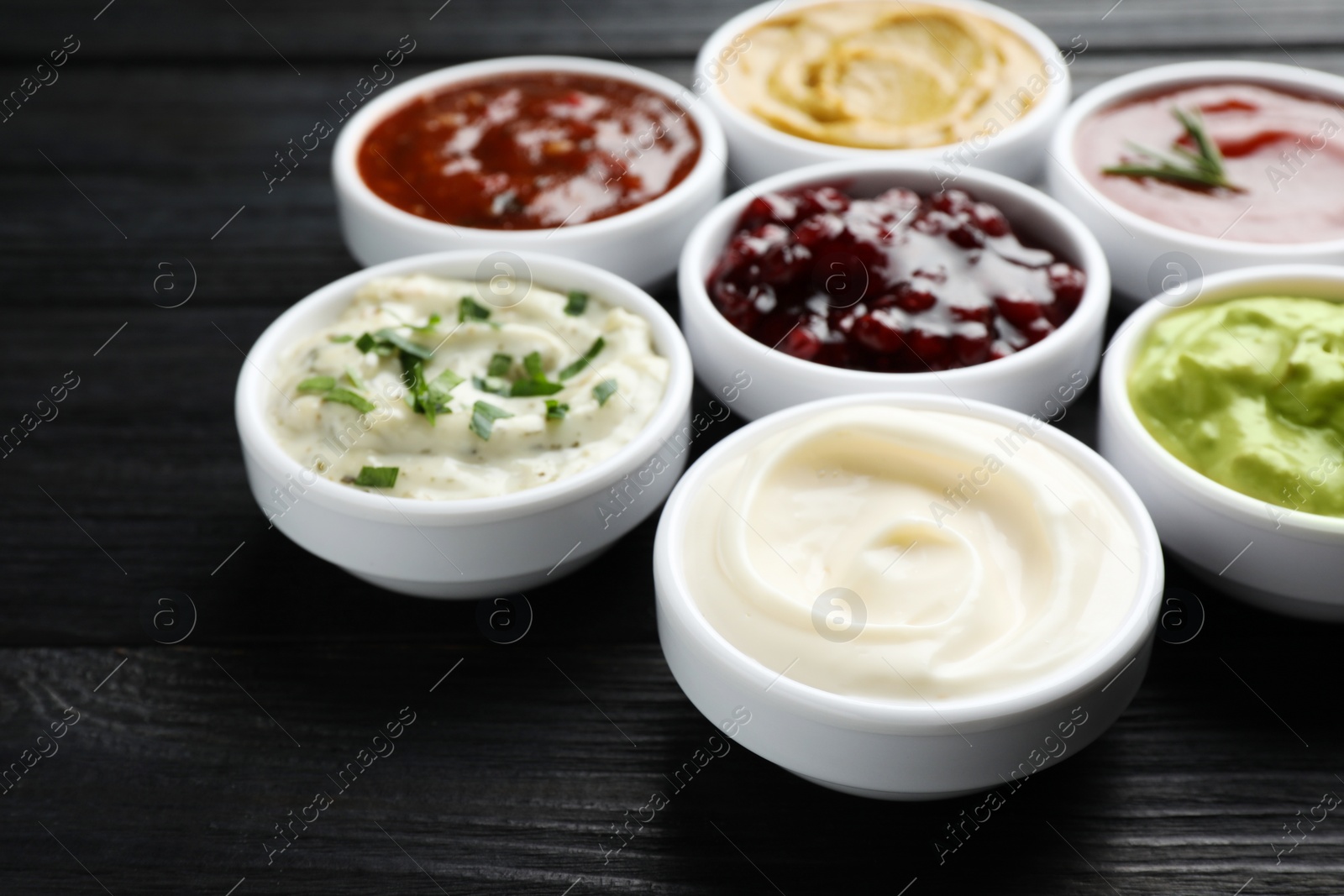 Photo of Different tasty sauces in bowls on black wooden table, closeup