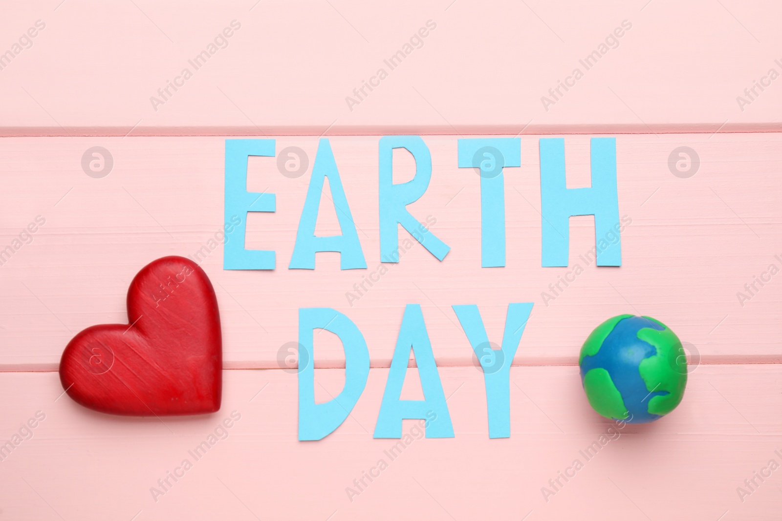 Photo of Words Earth Day, plasticine planet and decorative heart on pink wooden table, flat lay