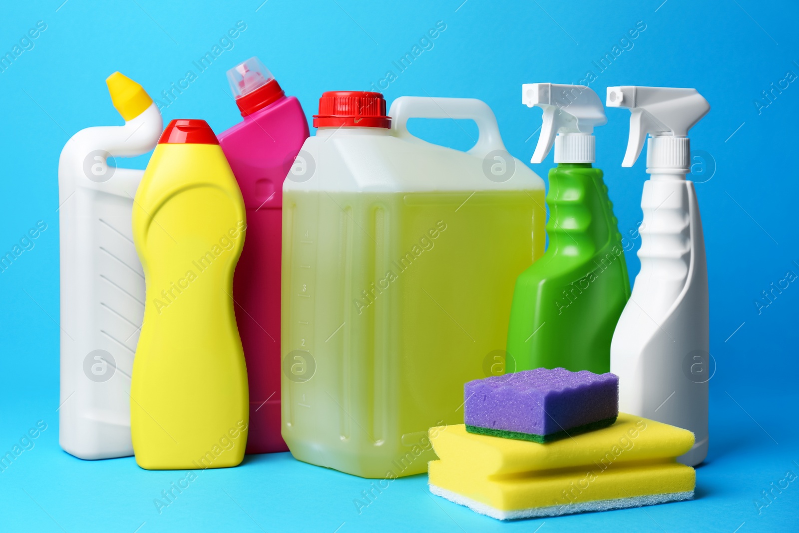 Photo of Bottles of detergents and sponges on light blue background. Cleaning supplies