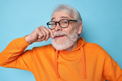 Photo of Senior man touching mustache on light blue background