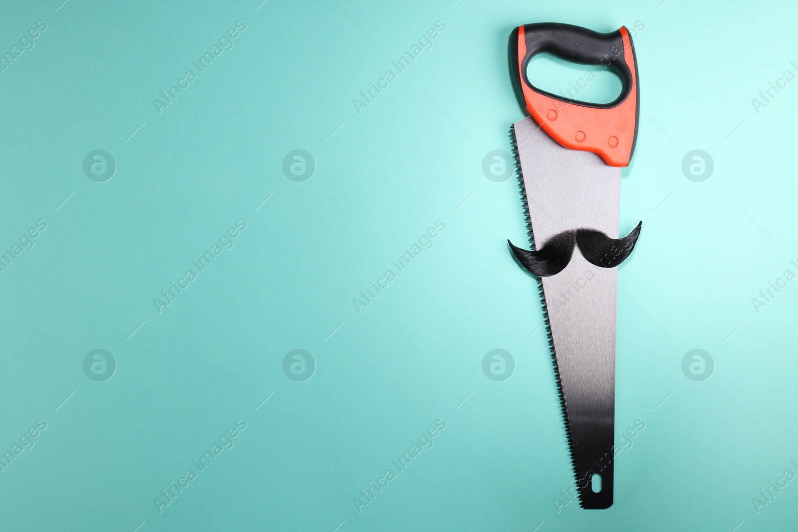 Photo of Man's face made of artificial mustache and hand saw on light blue background, top view. Space for text