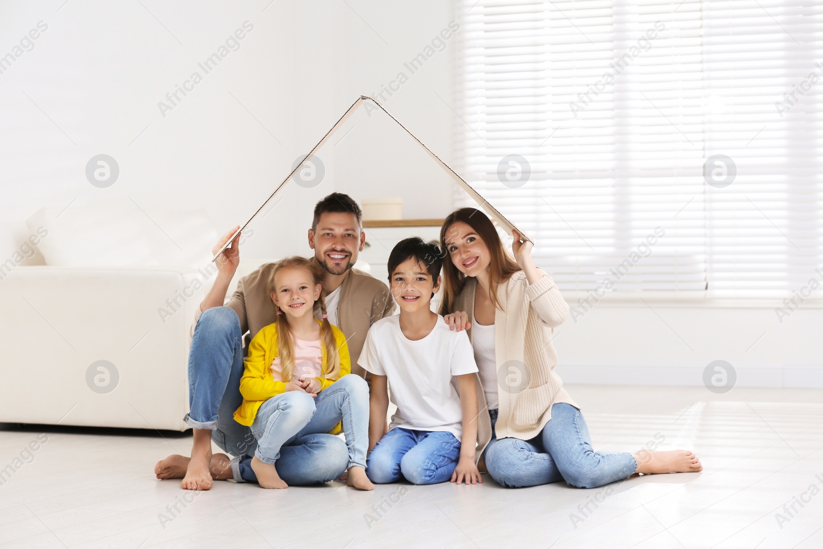 Photo of Happy family sitting under cardboard roof at home. Insurance concept