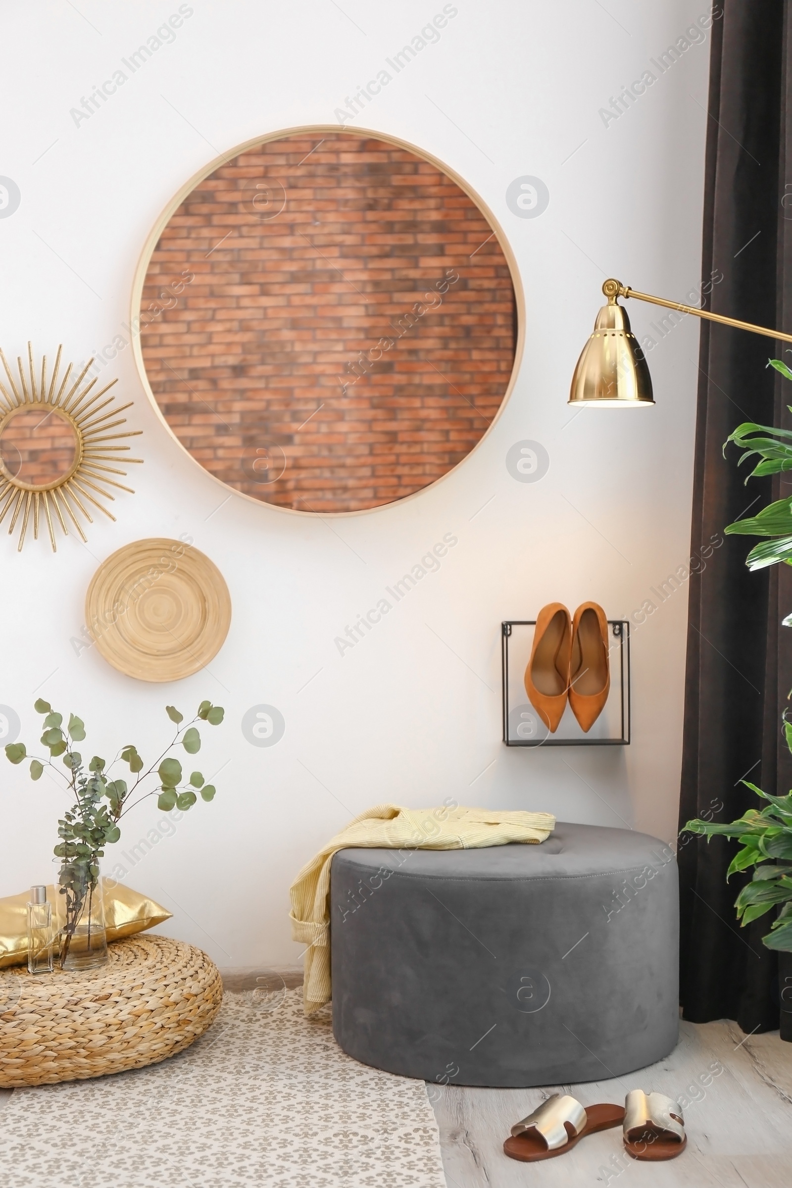 Photo of Hallway interior with big round mirror and ottoman chair near white wall