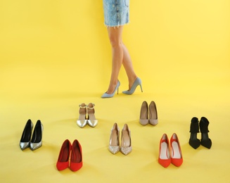 Photo of Woman trying on different high heel shoes on yellow background, closeup