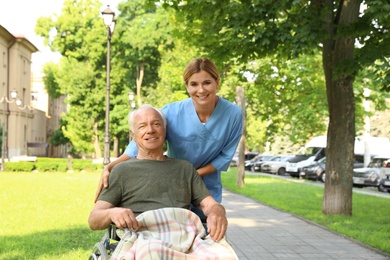 Photo of Happy nurse assisting elderly man in wheelchair at park