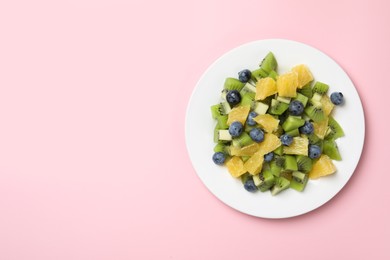 Plate of tasty fruit salad on pink background, top view. Space for text