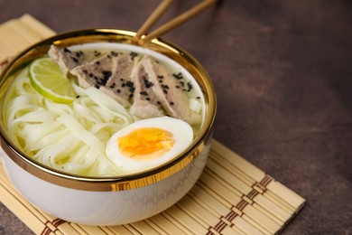 Photo of Bowl of delicious rice noodle soup with meat and egg on brown table, closeup. Space for text