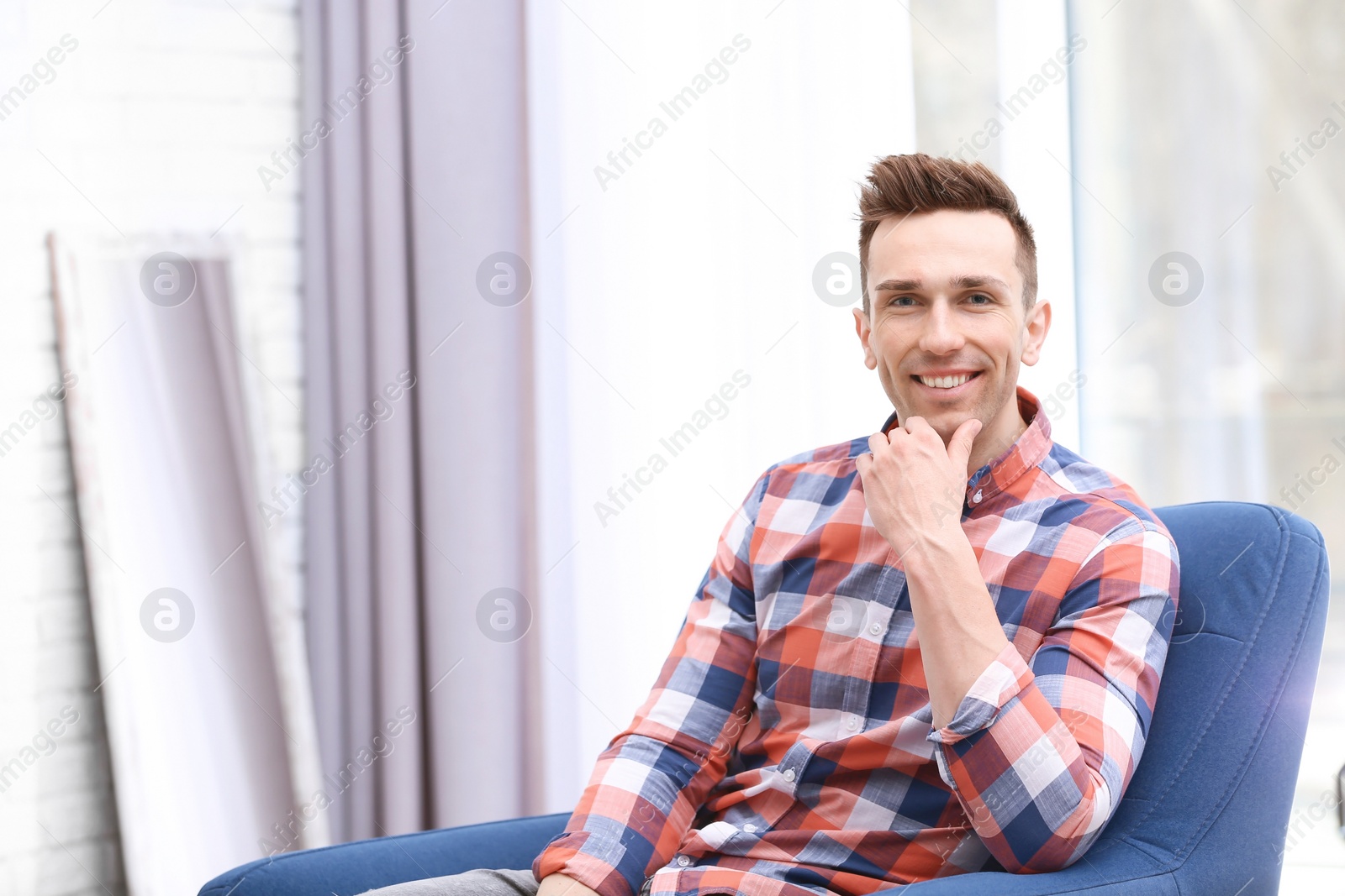 Photo of Young man sitting in armchair at home