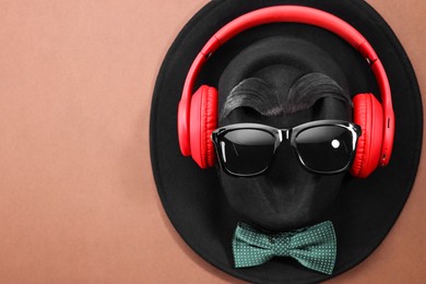 Photo of Man's face made of artificial mustache, sunglasses and hat on brown background, top view. Space for text