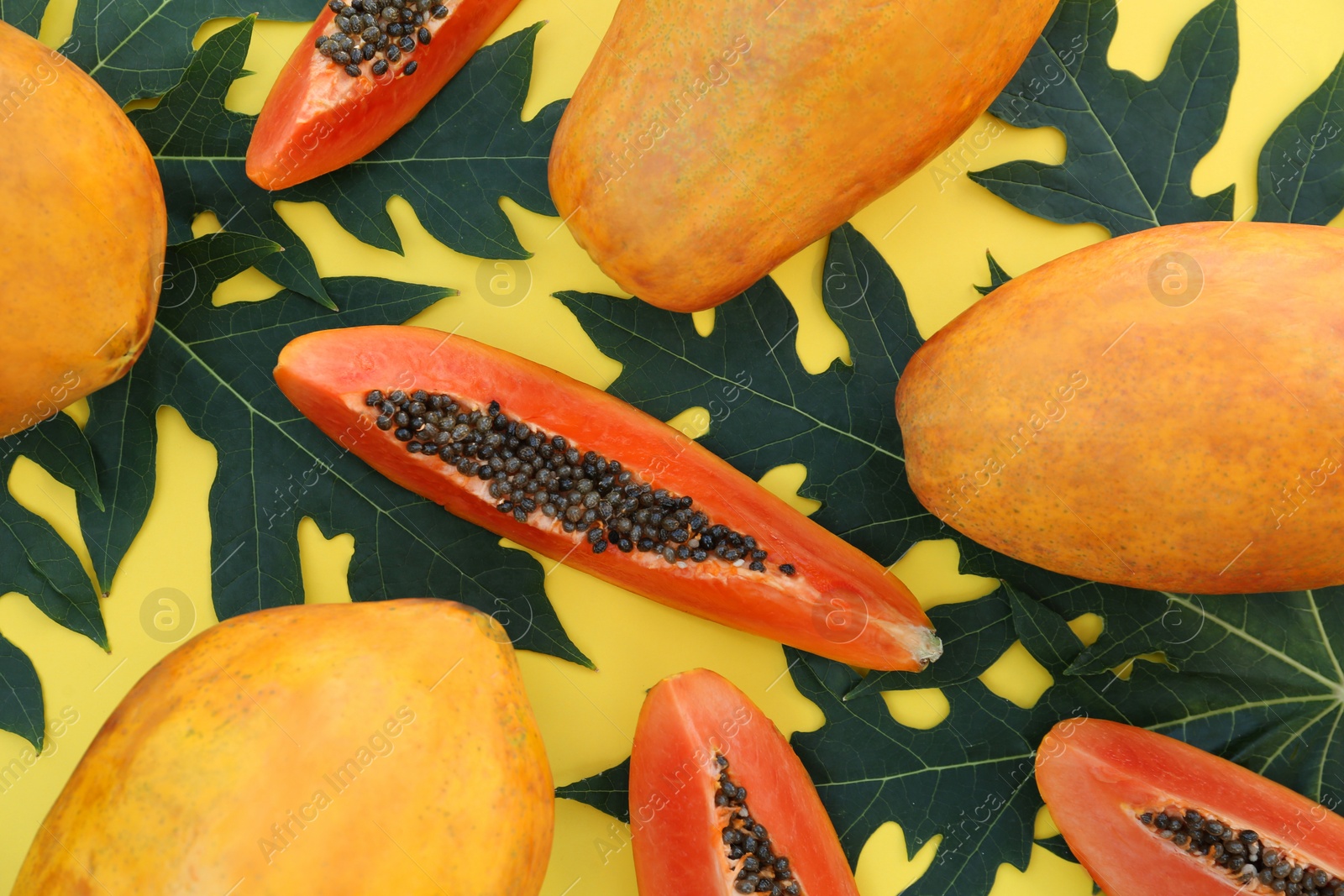 Photo of Fresh ripe cut and whole papaya fruits with leaves on yellow background, flat lay