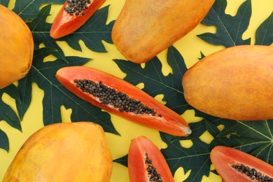 Fresh ripe cut and whole papaya fruits with leaves on yellow background, flat lay