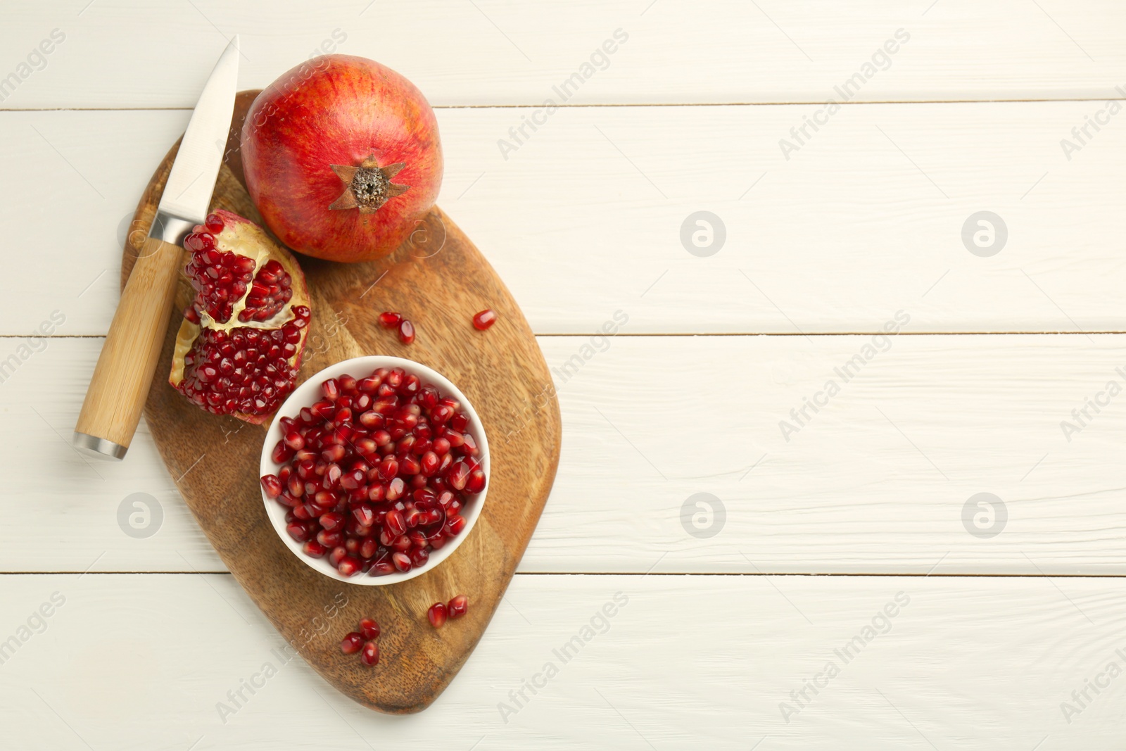 Photo of Ripe juicy pomegranate with grains and knife on white wooden table, top view. Space for text