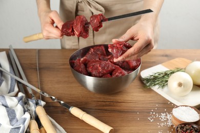 Woman stringing marinated meat on skewer at wooden table, closeup