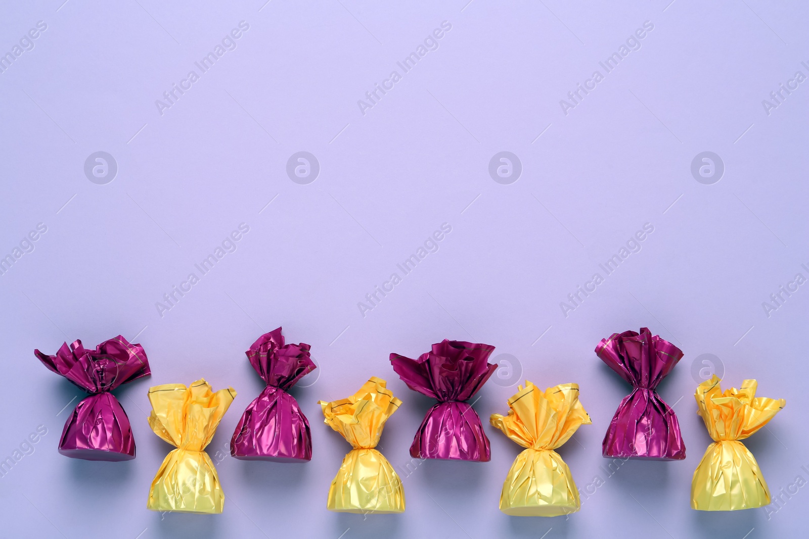 Photo of Candies in colorful wrappers on pink background, flat lay. Space for text