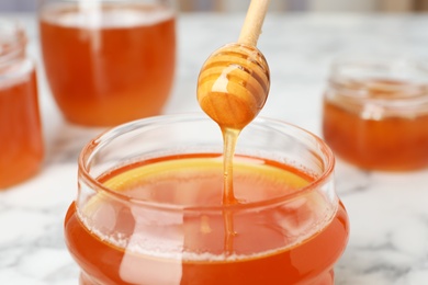 Photo of Sweet honey dripping from dipper into glass jar, closeup