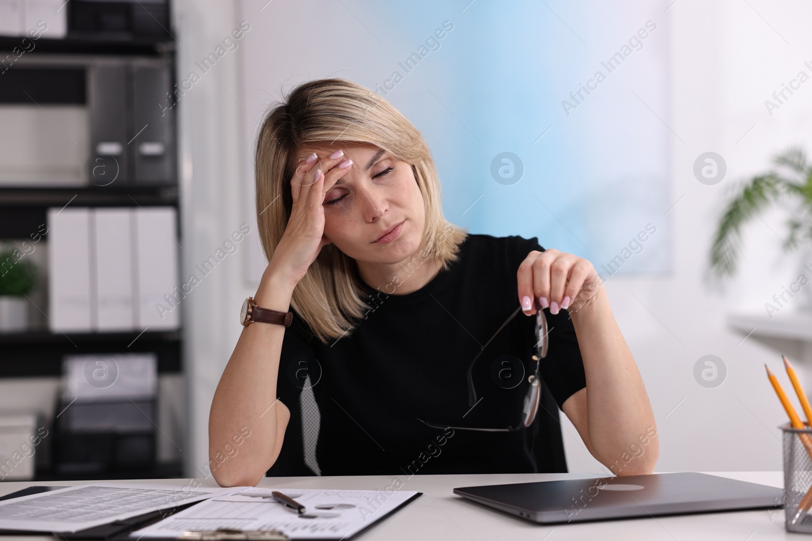 Photo of Overwhelmed woman with glasses sitting at table in office