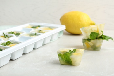 Photo of Ice cubes with mint and lemon near tray on table