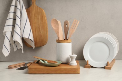 Set of different kitchen utensils and plates on white near gray wall
