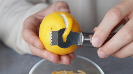 Man peeling fresh lemon with zester, closeup view