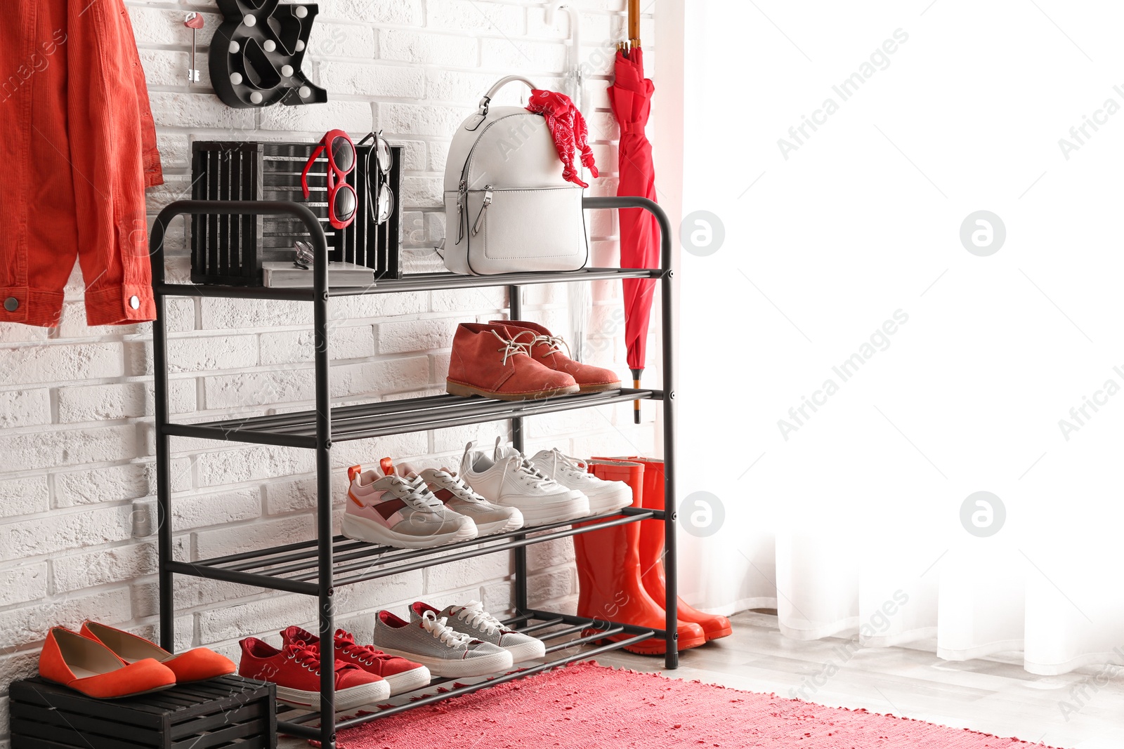 Photo of Shelving rack with stylish women's shoes and accessories near white brick wall indoors