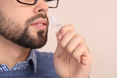 Photo of Man using nasal spray on beige background, closeup. Space for text