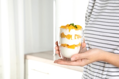 Photo of Woman holding glass of tasty peach dessert with yogurt in kitchen, closeup. Space for text