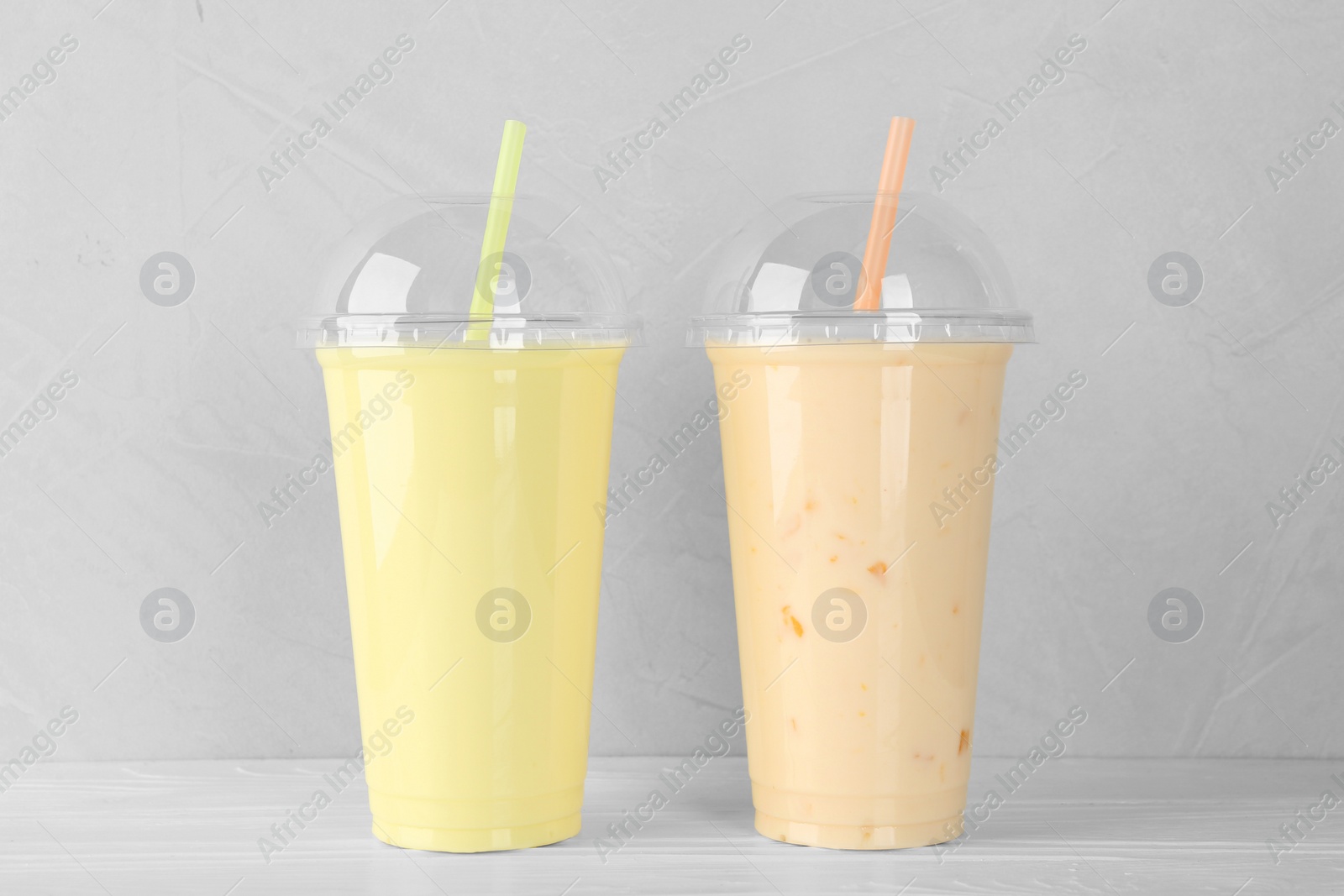 Photo of Plastic cups of different tasty smoothie on white wooden table